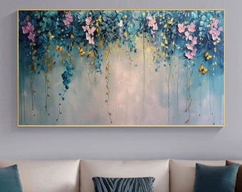 May include: A framed floral painting with a gold border. The artwork features cascading blue and green leaves, pink flowers, and gold accents. The background has a textured, light blue and white appearance. The painting is displayed above a white sofa with decorative pillows.