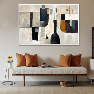 May include: Abstract art print in a white frame. The artwork features a geometric design with black, beige, and blue shapes. The painting hangs above a white bench with orange pillows. A small side table with a sunflower is to the left.