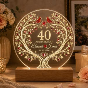 May include: A circular acrylic light display on a wooden base featuring an etched tree with two red cardinals at the top. The text reads 40 ANNIVERSARY, Eleanor and James, and 11.15.1986, accented with small red heart-shaped crystals.