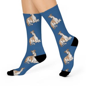 May include: Blue socks featuring a repeating pattern of a tan and white dog illustration. The socks have black heels and toes. The dog illustrations are in a relaxed, seated position.
