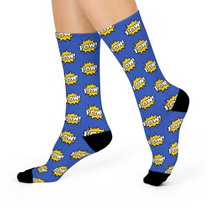 May include: Blue socks with a repeating pattern of yellow "POW!" text inside yellow starbursts. The socks have black heels and toes. The socks are worn on a person's legs.