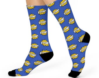 May include: Blue socks with a repeating pattern of yellow "POW!" text inside yellow starbursts. The socks have black heels and toes. The socks are worn on a person's legs.