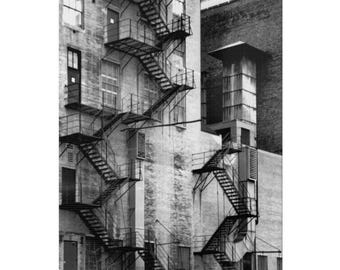 Könnte beinhalten: Schwarzweißfoto eines Backsteingebäudes mit mehreren Feuertreppen. Die Feuertreppen sind aus Metall und haben ein Kreuzmuster. Das Gebäude ist hoch und hat viele Fenster.
