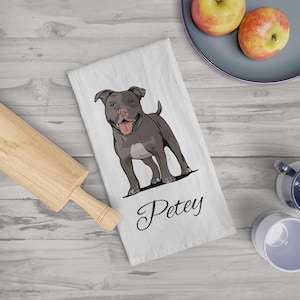 May include: White kitchen towel featuring a gray pit bull illustration with the name "Petey" in cursive script. The dog is depicted with its tongue out. The towel is on a light wood surface.