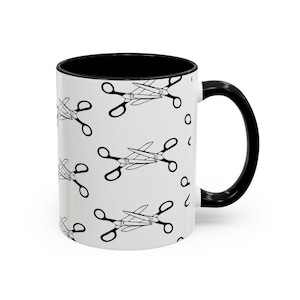 May include: White ceramic mug with a black interior and handle. The mug features a repeating pattern of black scissors. The scissors are in a classic design, with the blades crossed and the handles looped.