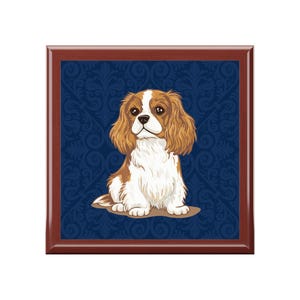 May include: A square wooden tray with a dark brown frame. The tray features a Cavalier King Charles Spaniel illustration on a dark blue background with a floral pattern. The dog is brown, white, and tan.