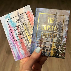 May include: Two books titled "The Crystal Forests" are shown. One is a guidebook with a colourful forest scene, the other is an intuitive card deck with a gold-framed forest design. The text is in gold and black.