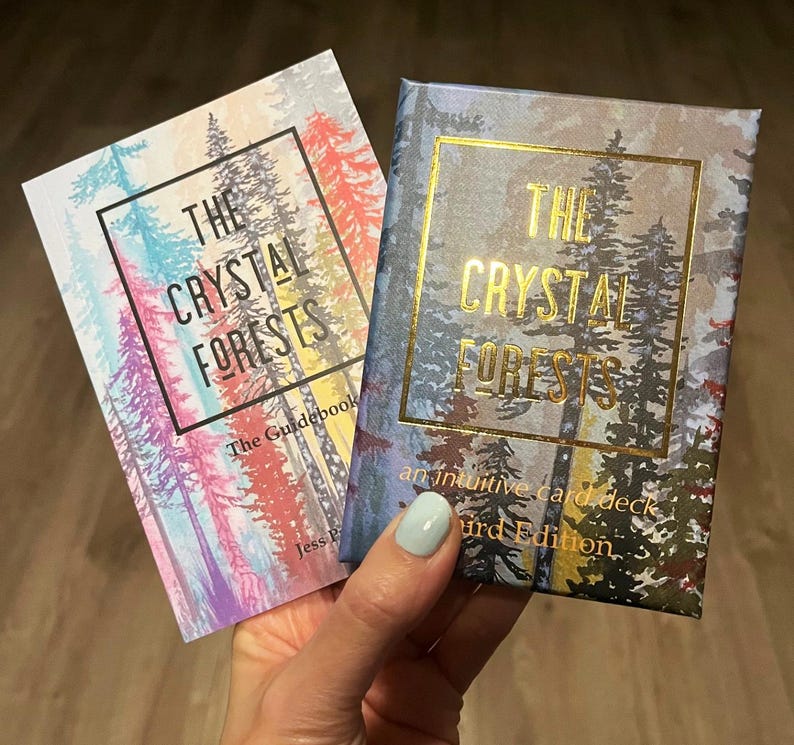 May include: Two books titled "The Crystal Forests" are shown. One is a guidebook with a colourful forest scene, the other is an intuitive card deck with a gold-framed forest design. The text is in gold and black.