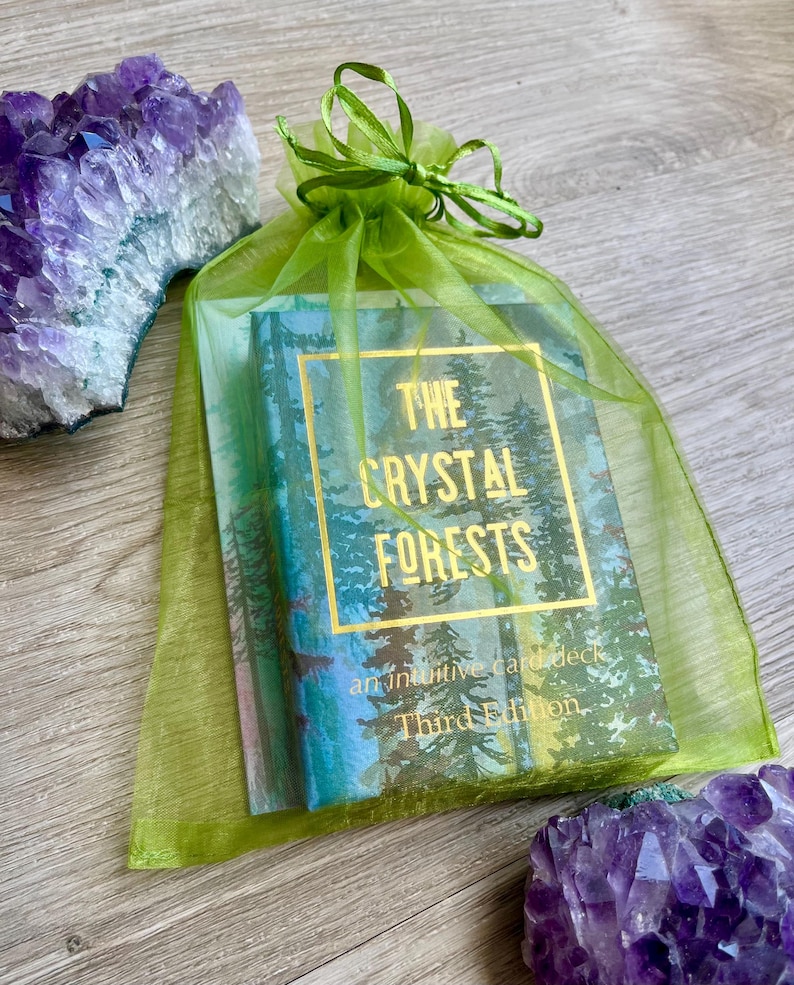 May include: A deck of "The Crystal Forests" intuitive cards in a green organza bag, with gold lettering and a forest scene. Amethyst crystals are visible on either side of the bag. The third edition is visible on the card deck.