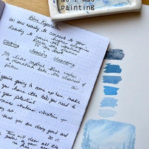 May include: A notebook with handwritten notes about Blue Kyanite, alongside blue watercolour paint swatches. The text "Blue Kyanite notes as I was painting" is at the top.