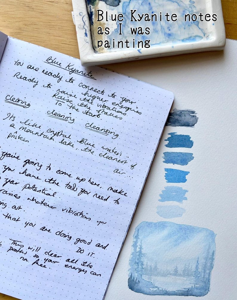 May include: A notebook with handwritten notes about Blue Kyanite, alongside blue watercolour paint swatches. The text "Blue Kyanite notes as I was painting" is at the top.