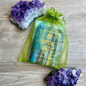 May include: Two amethyst crystal clusters and a deck of cards in a green organza bag. The card deck has a forest scene and the text "The Crystal Forests" in gold lettering. The crystals are a deep purple colour.