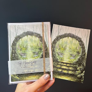 May include: A set of five postcards featuring a watercolor painting of a stone archway overgrown with greenery. The text "THE MOON GATE" and "5 POSTCARDS" is visible. The artist's name, "JESS PURSER ART", is also printed on the packaging.
