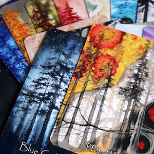 May include: A selection of rectangular cards with watercolour illustrations of trees in various colours. The cards feature names like "Blue Goldstone" and "Poppy Jasper". The artwork includes shades of blue, orange, red, and green.