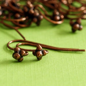 May include: A collection of copper-coloured metal earring hooks, each featuring a small, four-petaled flower-shaped stud at the end. The metal has a warm, burnished finish with a slightly darkened patina in the crevices of the floral design.