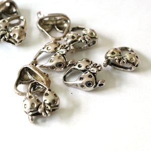 May include: Silver-coloured metal ladybird charms with a detailed design. The charms feature a ladybird with dotted wings and a loop for attaching to jewellery or other crafts. The charms are scattered on a white surface.