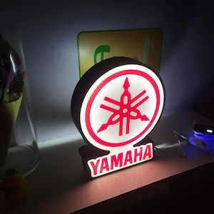 May include: A white and red Yamaha logo with the word "YAMAHA" in red letters below the logo. The logo is illuminated with white light.