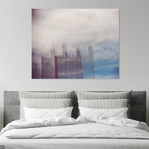 May include: A photograph of a city skyline with tall buildings obscured by a thick layer of fog. The buildings are a muted red color and the fog is a soft blue and white.