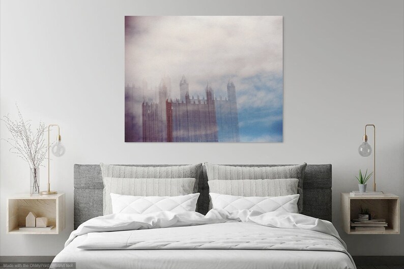 May include: A photograph of a city skyline with tall buildings obscured by a thick layer of fog. The buildings are a muted red color and the fog is a soft blue and white.