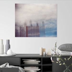 May include: A photograph of a city skyline with tall buildings obscured by a thick layer of fog. The buildings are a pale red color and the fog is a light blue and white color.