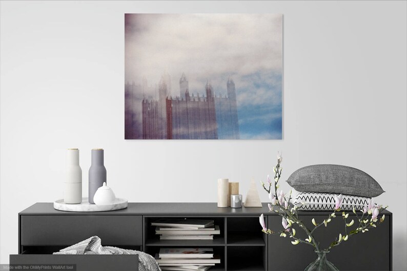 May include: A photograph of a city skyline with tall buildings obscured by a thick layer of fog. The buildings are a pale red color and the fog is a light blue and white color.