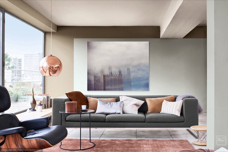 May include: A living room with a gray sofa, a coffee table, and a large framed print of a city skyline in the fog. The walls are painted in a light gray and a brown color. A copper globe pendant light hangs from the ceiling.