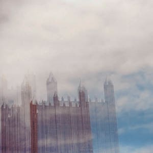 May include: A blurry image of a tall building with a cloudy sky in the background.