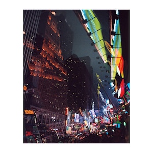 Può includere: Una vista notturna di una strada cittadina con edifici alti e luminosi cartelli al neon. I cartelli si riflettono nelle finestre degli edifici, creando un caleidoscopio di colori.
