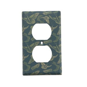 May include: A decorative electrical outlet cover with a teal background and a repeating pattern of stylized butterflies in shades of green and tan. The cover has two circular openings for the outlets and a small screw hole.