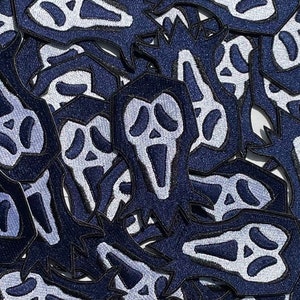 May include: A close-up of a pile of blue and white fabric patches featuring a ghost face design. The patches are made of a soft, textured fabric and have a black outline.