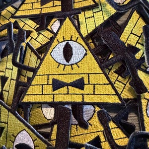 Puede incluir: Parches triangulares amarillos bordados con un patrón de ladrillos, un solo ojo y una pajarita negra. Los parches tienen bordes negros y están apilados. Los parches son adecuados para chaquetas, bolsos u otros artículos de tela.