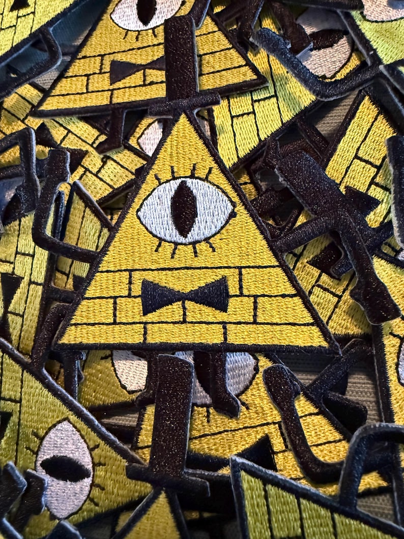 Peut inclure: &Eacute;cussons triangulaires jaunes brod&eacute;s avec un motif de briques, un seul &oelig;il et un n&oelig;ud papillon noir. Les &eacute;cussons ont des bordures noires et sont empil&eacute;s. Les &eacute;cussons conviennent aux vestes, sacs ou autres articles en tissu.