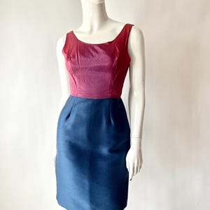 May include: A sleeveless, knee-length dress with a color-blocked design. The bodice is a deep burgundy, transitioning to a lighter pink hue. The skirt is a solid navy blue. The dress is displayed on a mannequin.