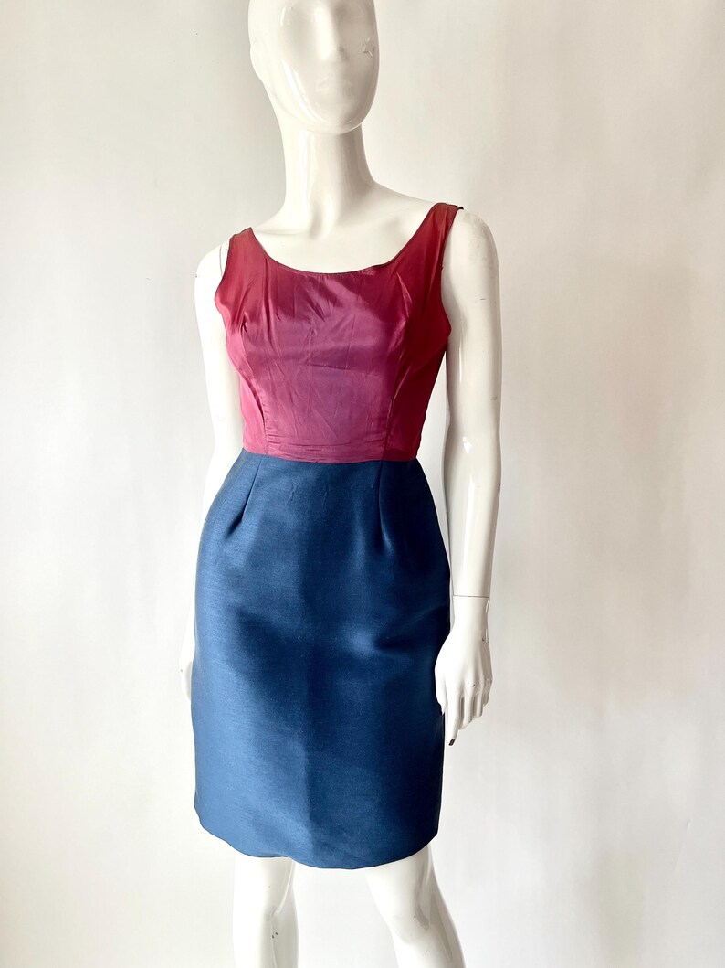 May include: A sleeveless, knee-length dress with a color-blocked design. The bodice is a deep burgundy, transitioning to a lighter pink hue. The skirt is a solid navy blue. The dress is displayed on a mannequin.