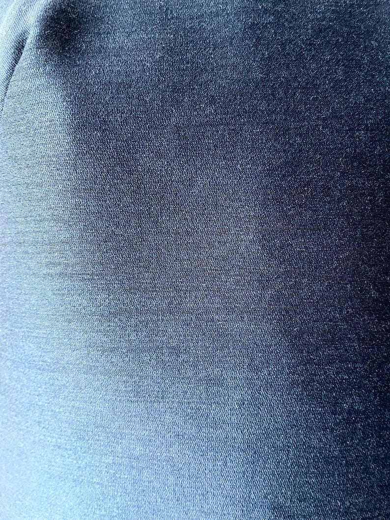 May include: Close-up of a textured, navy blue fabric. The material has a subtle sheen, with visible woven threads creating a slightly uneven surface. The color shifts slightly in the light, adding depth to the solid color.