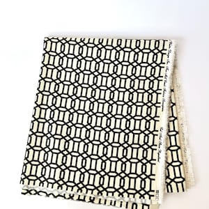 May include: Folded fabric with a geometric black and cream pattern. The design features interlocking shapes, creating a modern and stylish look. The fabric has a raw edge on one side, and the text "White Design for the Mill Creek Fabrics" is visible.