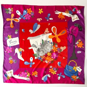 May include: A red, pink, and purple silk scarf with a floral pattern and a variety of whimsical designs, including butterflies, hats, shoes, gloves, and a handbag. The scarf features the word "Gucci" in cursive.