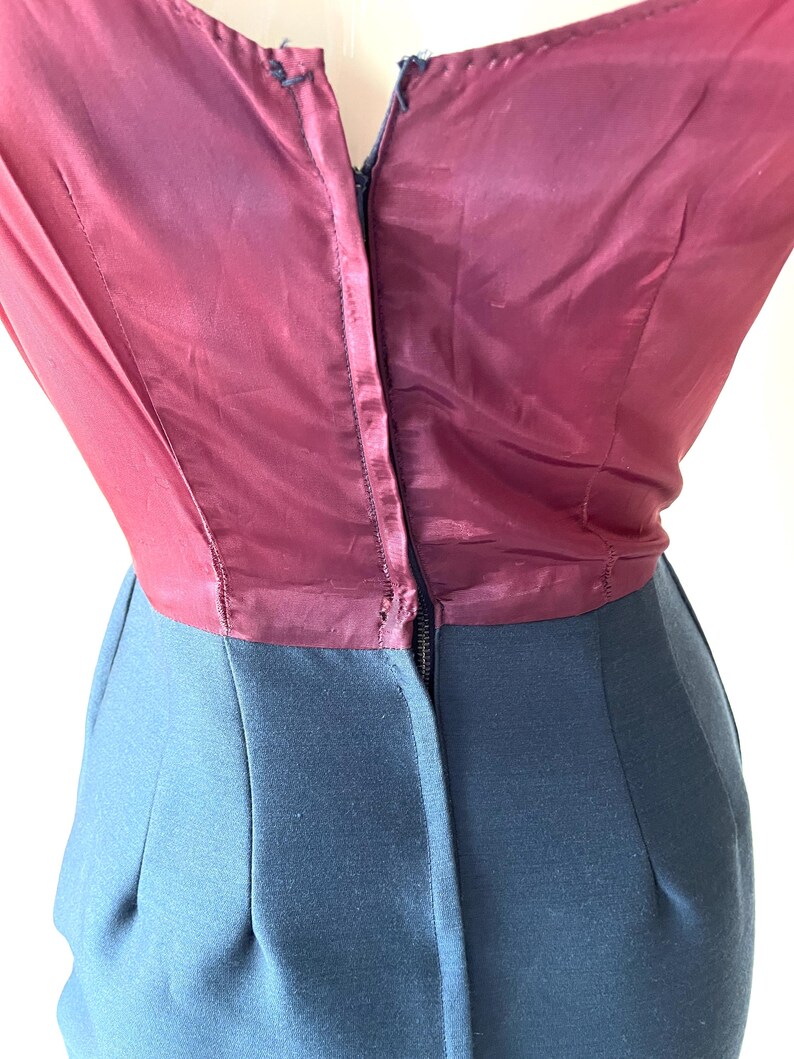 May include: A vintage dress featuring a burgundy silk bodice and a dark teal skirt. The bodice has a V-neckline and a zipper closure down the front. The skirt is a solid color with a tailored fit.