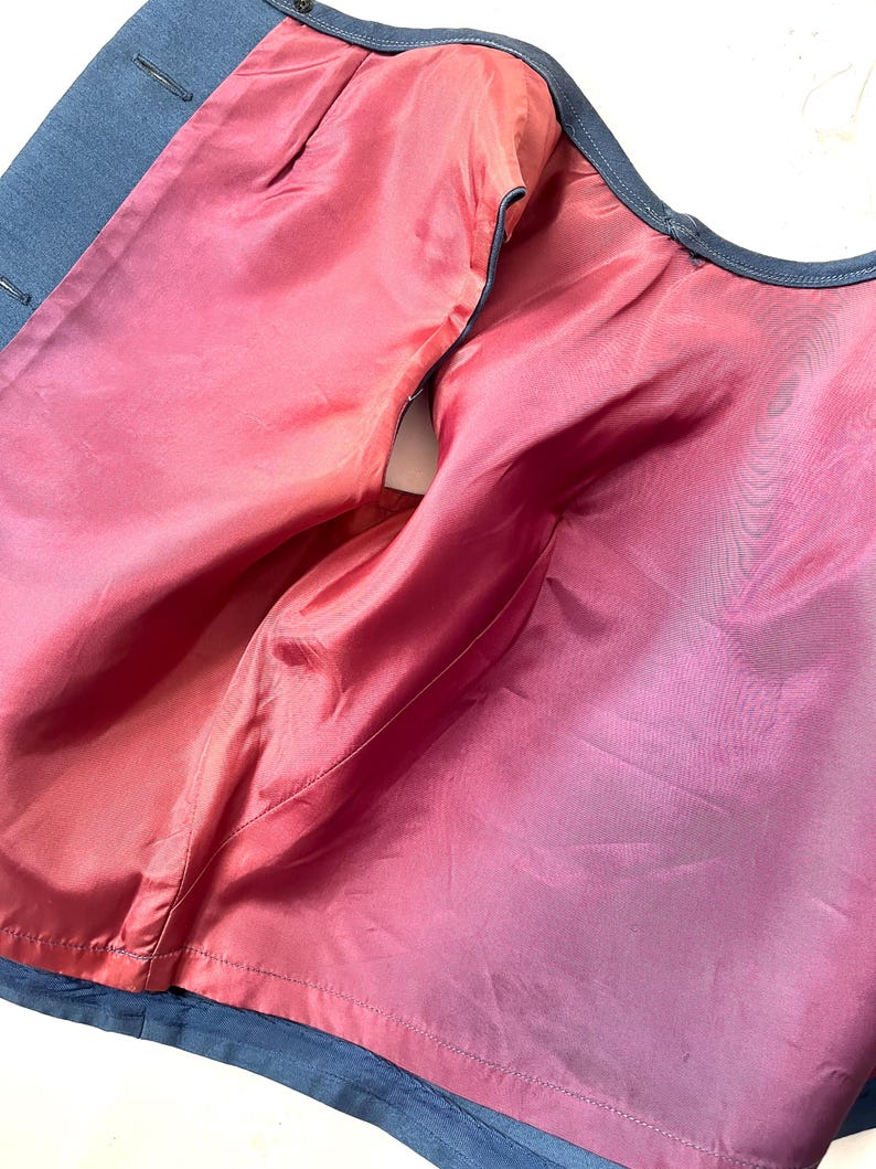 May include: A partially unbuttoned, dark blue blazer with a vibrant pink interior lining. The lining is a smooth, silky material, and the blazer's exterior has a subtle texture. The image highlights the contrast between the outer and inner fabrics.