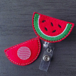 May include: A red and green watermelon-shaped badge holder with a clear plastic badge holder and a clear plastic button.