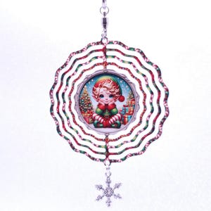 Puede incluir: Un móvil de viento con temática navideña que presenta una imagen central de un elfo de dibujos animados rodeado de regalos y un árbol de Navidad. El anillo exterior tiene un diseño de bastón de caramelo rojo, blanco y verde, con un dije de copo de nieve colgando.