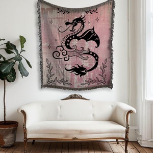 May include: A pink and black woven tapestry featuring a black silhouette of a dragon with a cloud and flames. The dragon is surrounded by floral vines and stars.