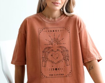 May include: A rust-colored t-shirt with a graphic of a tarot card depicting two skeletal hands forming a heart with a smaller heart inside. The card is titled "The Lovers".