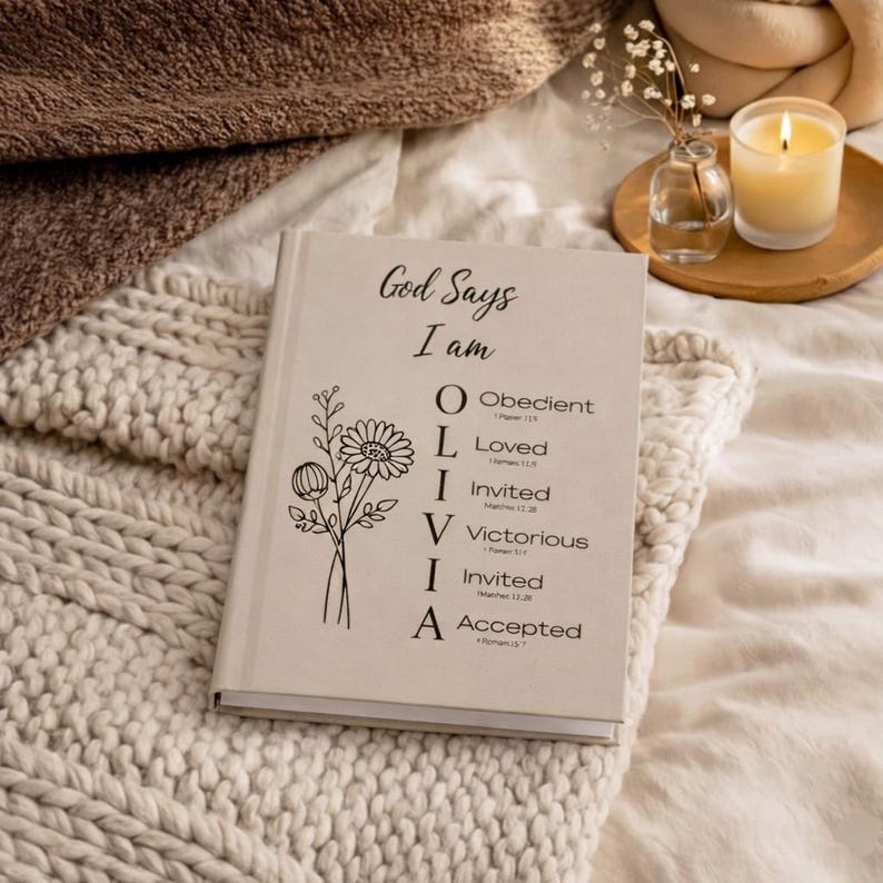 May include: A beige hardcover book with black text and a floral line drawing. The cover reads God Says I am OLIVIA, with O for Obedient, L for Loved, I for Invited, V for Victorious, I for Invited, and A for Accepted, each followed by a Bible verse.