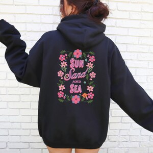 May include: Black hooded sweatshirt with a floral design and the text "Sun Sand and Sea" in pink lettering.