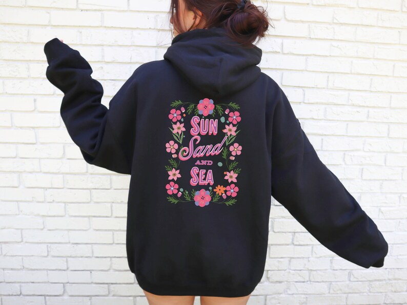 May include: Black hooded sweatshirt with a floral design and the text "Sun Sand and Sea" in pink lettering.