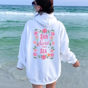 May include: White hoodie with a floral design and the text "Sun Sand and Sea" in pink lettering.