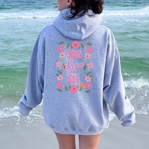 May include: Gray hooded sweatshirt with a floral design and the text "Sun Sand and Sea" on the back.
