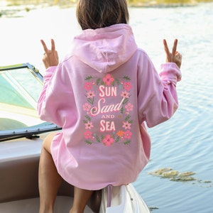 May include: Pink hoodie with a floral design and the text "Sun Sand and Sea" on the back.
