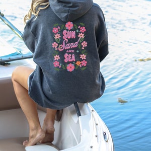 May include: A dark gray hooded sweatshirt with a floral design and the text "Sun Sand and Sea" on the back.